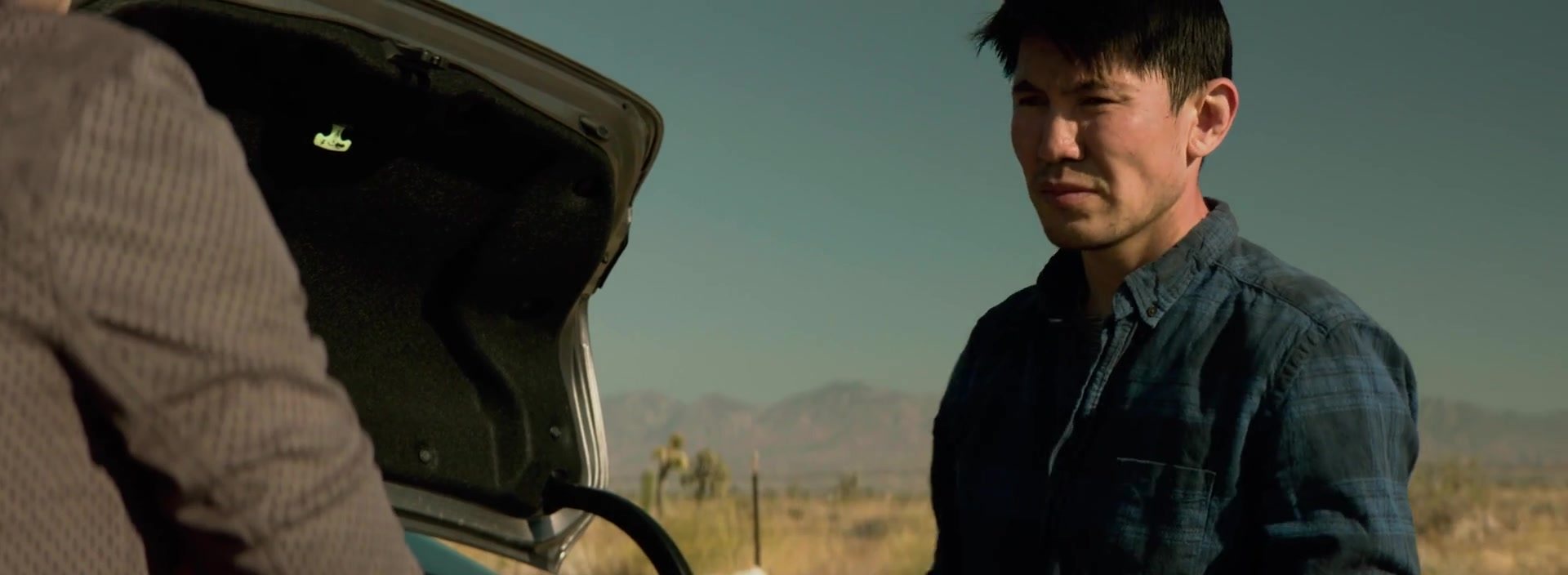 Medet Aman in The Final Stop, standing by an open car trunk on a desert road