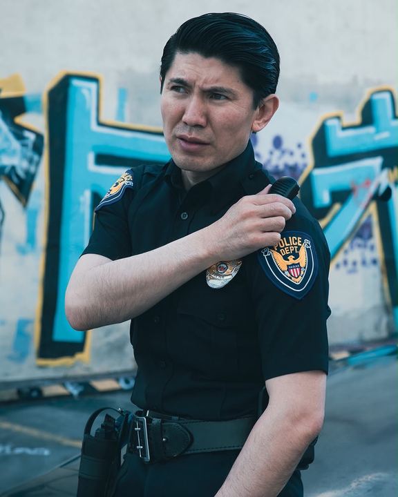 Medet in police uniform speaking into a shoulder radio in front of a graffiti wall