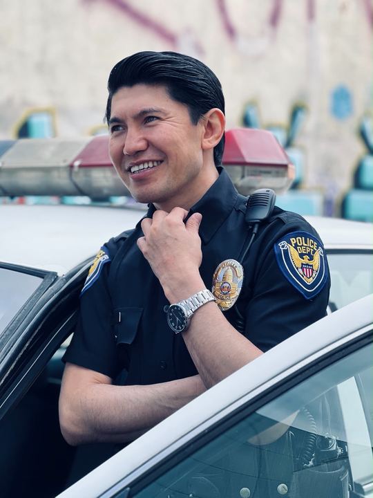 Medet in uniform smiling and leaning on a patrol car