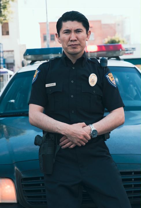 Medet standing in police uniform in front of a patrol car